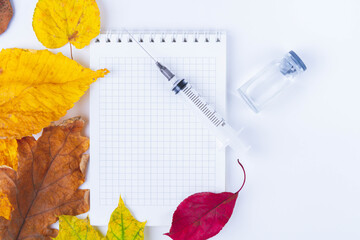 Vaccine and syringe are on table next to doctor's notebook and autumn leaves. Blank notebook for notes in doctor's office. Autumn vaccination..