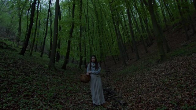 Woman in white dress stands in woods carrying basket on a calm day