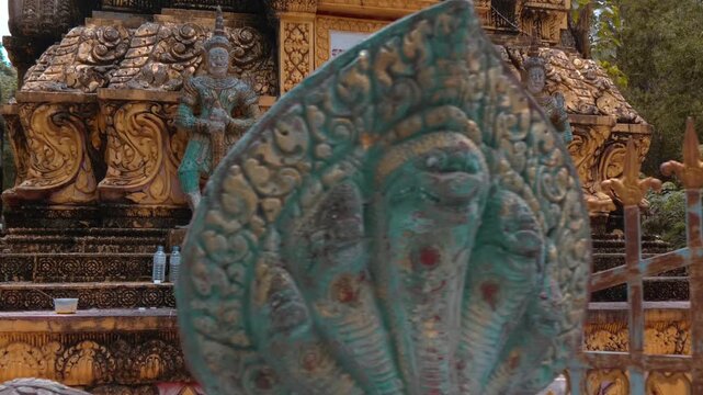 Massive golden stupa with statues of Yakshas demon guardians on its levels stand in the temple grounds of Wat Svay Romeat Pagoda in Siem Reap, Cambodia. Shot in motion