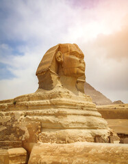 Ancient sphinx sculpture against a cloudy sky and pyramids in the distance