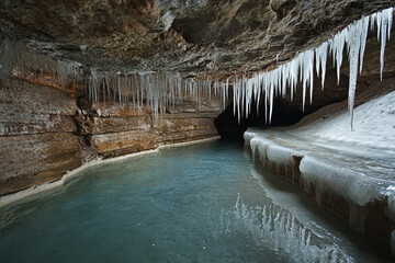 A frozen underground river with icicles hanging from the cavern ceiling