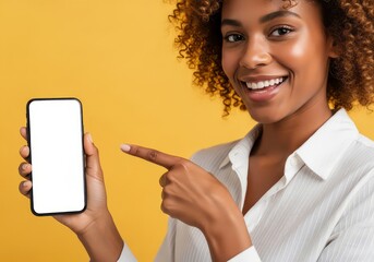 Smiling young woman with curly hair pointing at a smartphone with a blank white screen, isolated on a yellow background, showcasing a mobile app or website