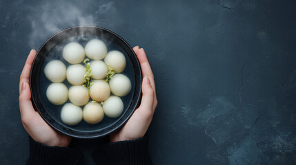 Hands holding steaming bowl of tangyuan glutinous rice balls for Dongzhi Festival winter solstice celebration