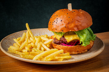 A juicy hamburger with cheese and a side of French fried potatoes are on a plate