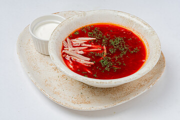 A vibrant red beet soup is presented with meat slices and dill, next to white sour cream