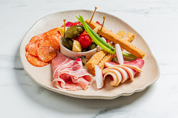 Selection of meats, pickled vegetables, and breadsticks presented on an artistic plate