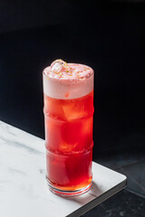 A red cocktail with a creamy top sits on a marble surface. It looks delicious and refreshing