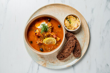 A flavorful Solyanka soup is presented with rye bread and spread, resting on a stone plate