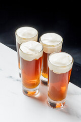 Several glasses filled with amber liquid and topped with white foam sit on a marble counter