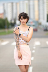 Young woman with short hair and floral crop top poses confidently on urban street, showcasing modern fashion style and vibrant city atmosphere with blurred background