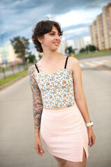 Young woman with short hair and floral crop top poses confidently on urban street, showcasing modern fashion style and vibrant city atmosphere with blurred background