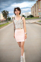 Obraz premium Young woman with short hair and floral crop top poses confidently on urban street, showcasing modern fashion style and vibrant city atmosphere with blurred background