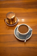 Close-up of a cup of coffee and metal phin filter on a wooden table, warm café style beverage