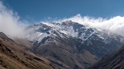 Snow capped mountain peaks under a bright blue sky with swirling clouds obscuring some slopes