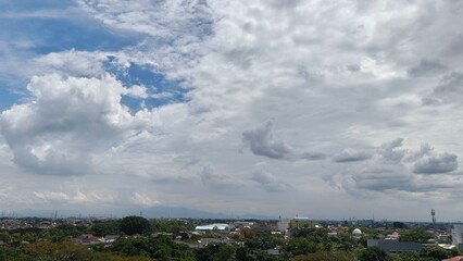 Obraz premium Dramatic cloudscape over a city with trees, showcasing a beautiful daytime sky with fluffy clouds