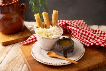 Flautas Ahogadas (Drowned Flautas) Golden tacos made with fried corn tortillas, filled with chicken or beef, and served in a glass or cup containing salsa or broth, lettuce, sour cream, and cheese.