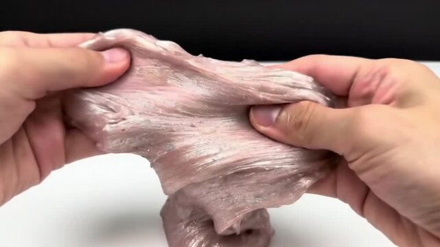 Hands stretching and playing with a beige glitter slime on a white background indoors