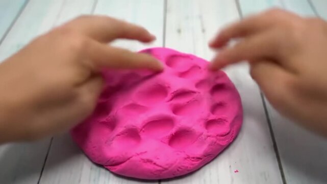 Close up of hands poking and playing with a pink, soft, and moldable clay material