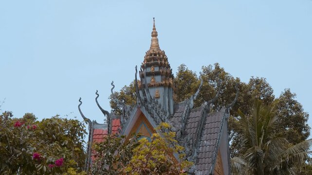 Tiled roof of Wat Svay Romeat Pagoda with traditional chofahs and a gable against the sky. Shot in motion