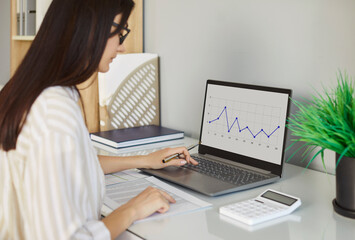 Focused businesswoman manages laptop and documents for online business accounting working in office, mastering financial audit, anchoring a professional space where dedication and economic precision.