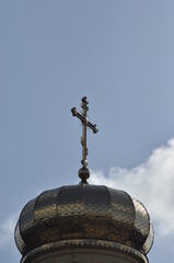 Cross atop a golden dome against a clear blue sky on a sunny day in a religious setting