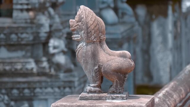 An old stone statue of a snow lion or Singha stand on a parapet against the background of Buddhist stupas in the Wat Svay Romeat Pagoda grounds in Siem Reap, Cambodia. Shot in motion