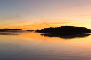 Golden sunrise over calm autumn sea with forest on the shore and gentle fog above the water, peaceful natural seascape and morning atmosphere