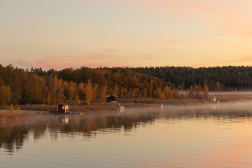 Golden sunrise over calm autumn sea with forest on the shore and gentle fog above the water, peaceful natural seascape and morning atmosphere
