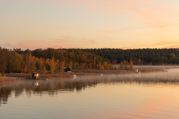 Golden sunrise over calm autumn sea with forest on the shore and gentle fog above the water, peaceful natural seascape and morning atmosphere