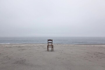 Lonely wooden chair facing a quiet sea under a gray sky at dusk Generative AI