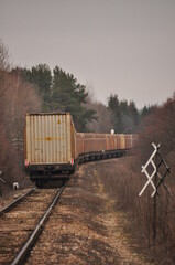Obraz premium Cargo train travels along a winding railway surrounded by trees on a cloudy day