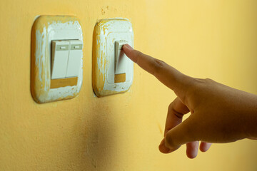 A human hand pressing a light switch on a yellow wall, symbolizing saving energy and controlling electricity at home, landscape