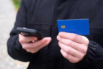 The businessman holds a smartphone and a blue bank card, making a payment and entering bank details. the danger of the Internet and data protection.