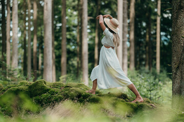 Woman in flowing white dress practices yoga on moss wall in forest absorbing peace from nature&rsquo;s silence and grounding energy