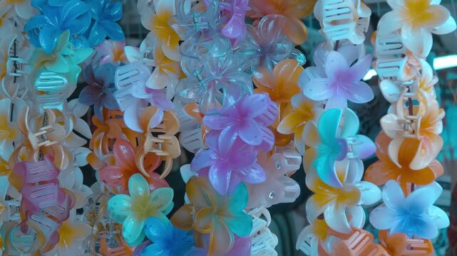 A large selection of beautiful, colorful flower-shaped plastic women's hairpins hang at a market in Siem Reap, Cambodia. Closeup. Shot in motion