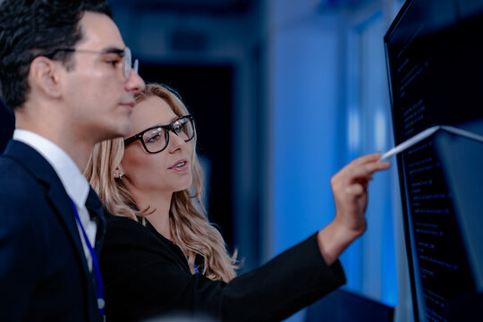 Validating the future AI. A specialist points out a crucial parameter in an AI model's code displayed on screen discussing its ethical implications with her colleague before deployment.