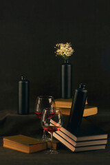 Still life with books, flowers, glasses of wine and black bottles