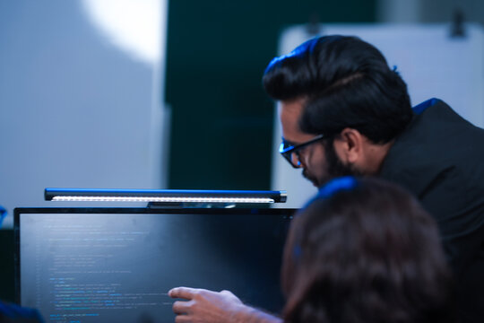 Deep code analysis huddle late night. Senior developer points out intricate logic colleague absorbs critical details screen reflects complex script intense debugging session proceeds now code work.