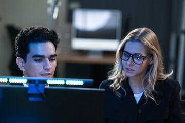 Dynamic tech team collaborates late night. Young Asian woman points at screen explaining project...