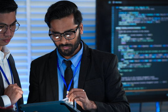 AI research team huddles late night innovators review complex machine learning model architecture discuss training data using tablet stylus futuristic lab code screens glow bright.