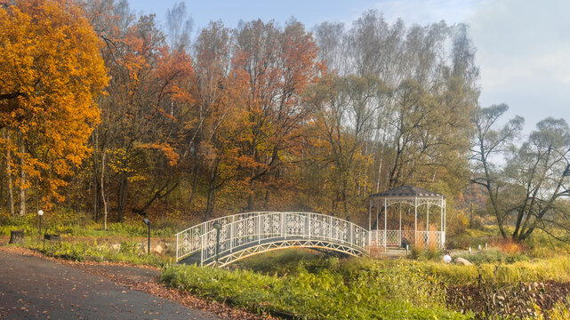 White bridge to gazebo in a city park in autumn scenery.