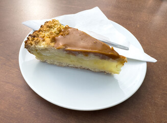 Slice of caramel apple pie on white plate with fork on wooden table