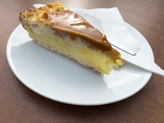 Caramel apple pie slice on white plate with napkin and fork on wooden table