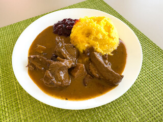 Savory venison stew with mashed potatoes and lingonberry sauce on a green placemat