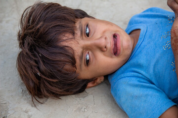 Poor Pakistani village girl crying on dusty ground, sad child expressing pain and emotion in rural...