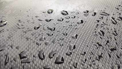 Close-up makro tetesan air yang membentuk manik-manik di permukaan kain tenun gelap antiair. Mewakili teknologi tahan air, tekstur, perlindungan, dan dinamika fluida.