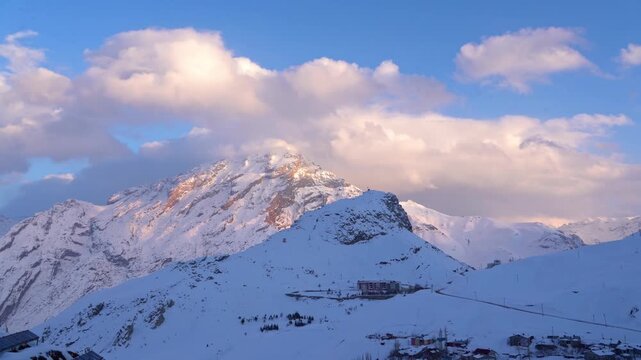 Cinematic view of snowy Mount Sumbul in Hakkari at sunset, majestic snow-capped mountain peaks under blue sky with clouds, winter landscape in Eastern Turkey, 4K 25fps. 1