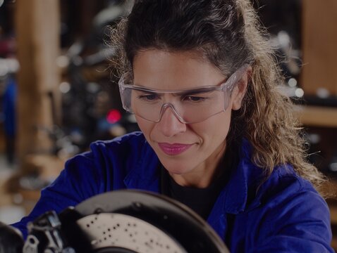 Female auto mechanic working on a car brake system in a well-lit garage during daytime