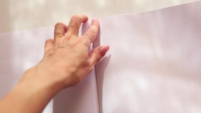 Close-up of female hands tearing a blank white sheet of paper out of a spiral notebook. The action is dynamic and focused, symbolizing a new start, a mistake, or a creative impulse
