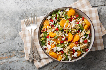Diet quinoa salad with spinach, feta, tangerines, pomegranate, and pistachios dressed with a lemon-yogurt sauce, close-up in a bowl on a table. Horizontal top view from above
